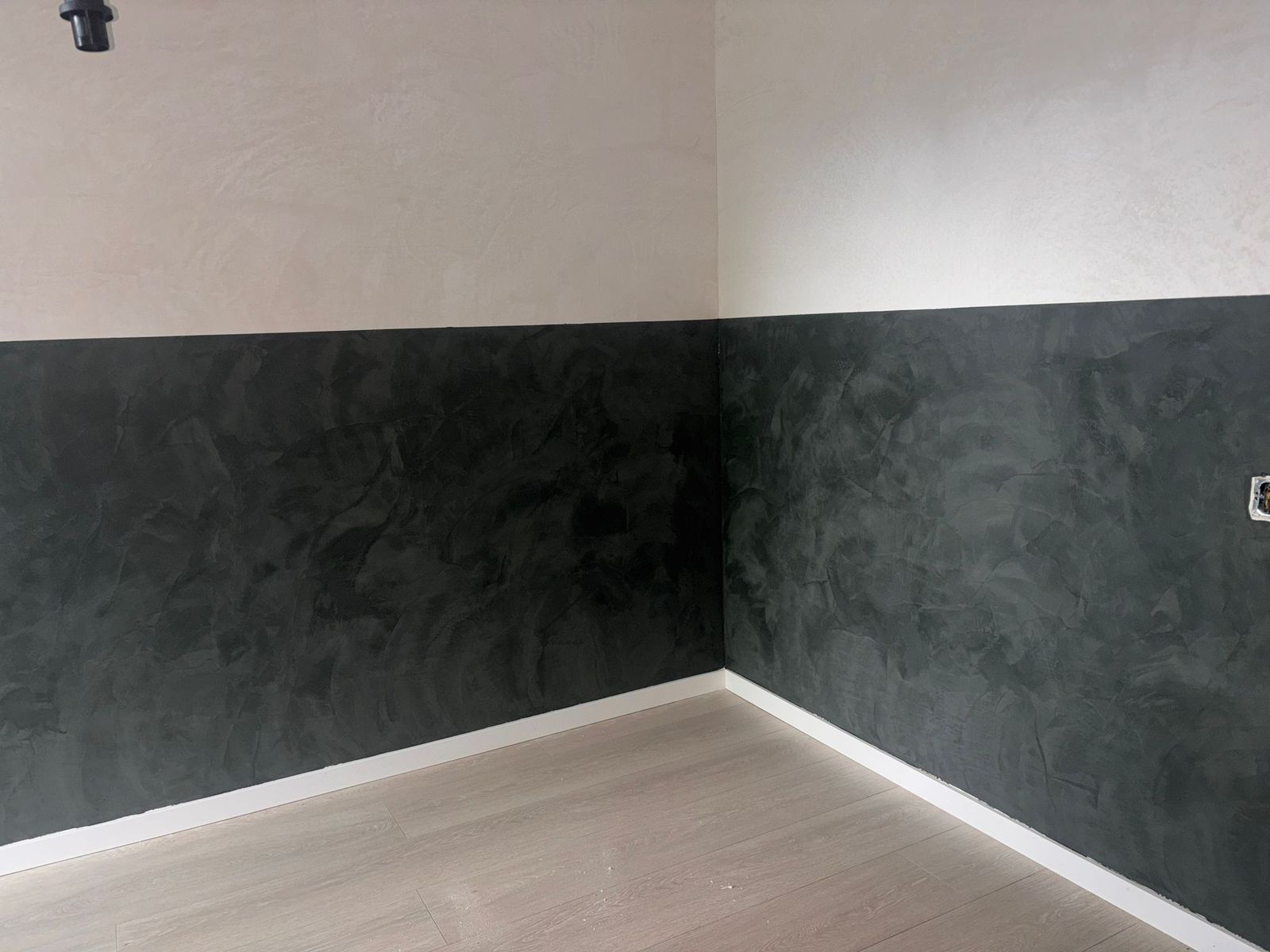 Een kamer met een donkere, met de spaan gezette onderwand en een lichte gestucte bovenwand