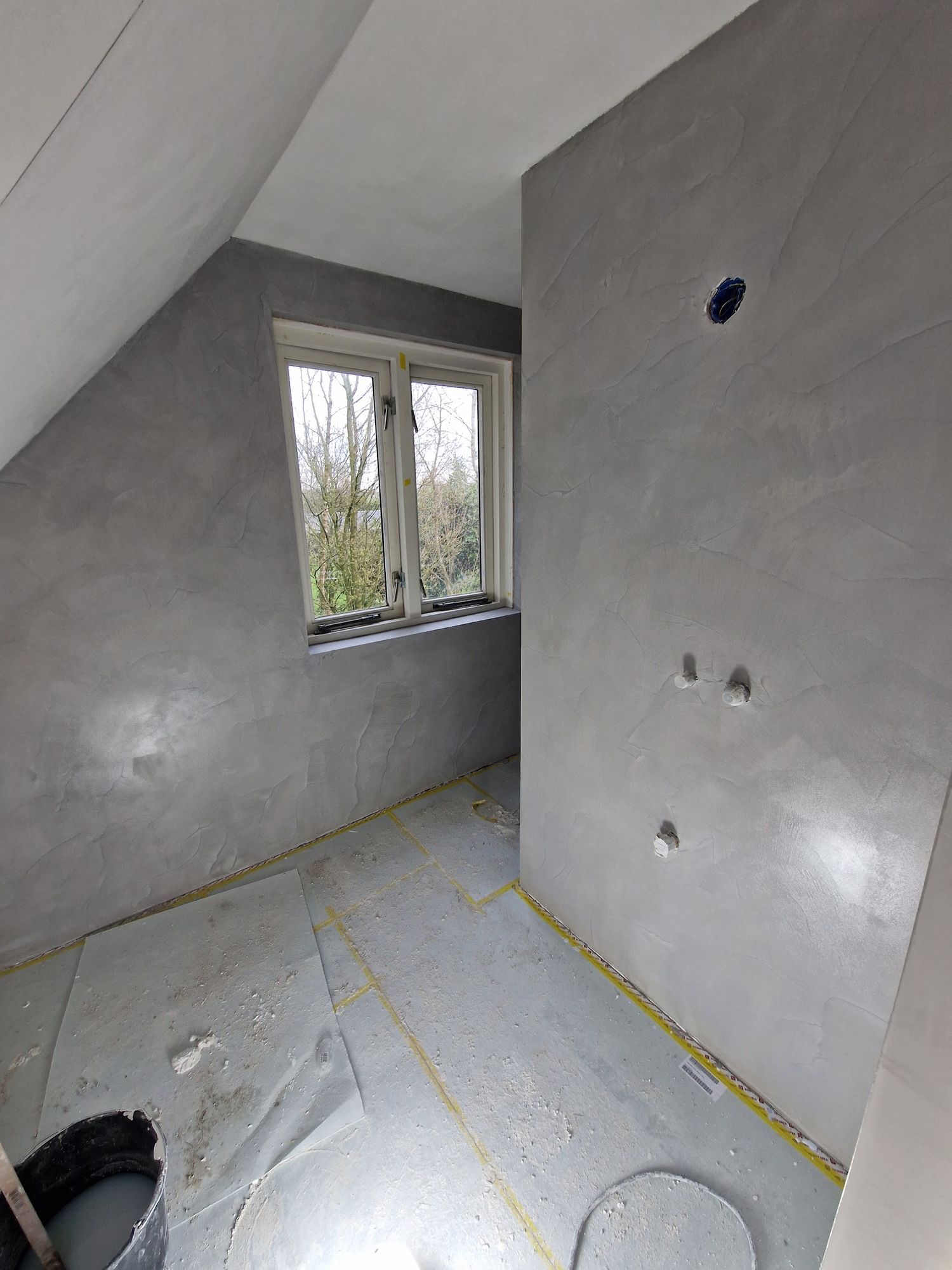 Een zolderkamer met grijze, wolkig afgewerkte wanden rond het raam